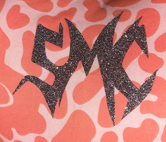 Close-up of the SMC sigil in a sparkly black vinyl, heat-applied to a coral and pink heart animal print fabric — a signature design element from Sam’s Mystic Collection.
